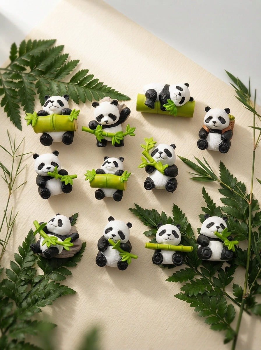 Set of hand-finished panda miniatures arranged on a warm cream desk surface with forest green plants and bamboo accents.